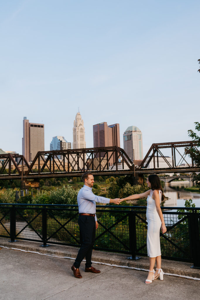 Morgan and Mitch dancing near the waterfront at North Bank Park with the Columbus skyline in the background.